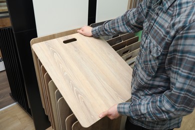 Photo of Man with sample of wooden flooring in shop, closeup