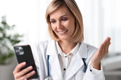 Photo of Smiling doctor with smartphone having online consultation in office