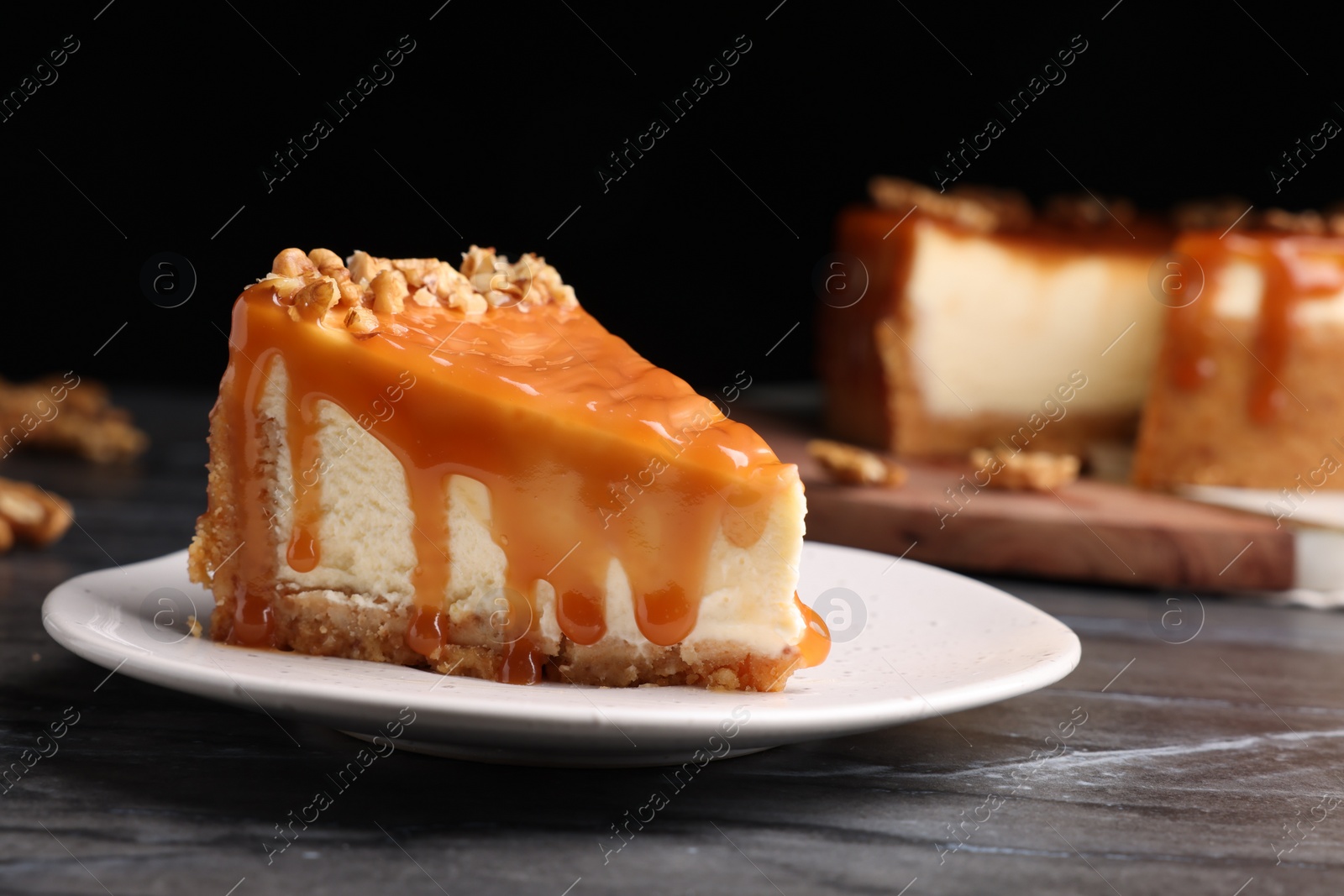 Photo of Piece of delicious cake with caramel and walnuts on black marble table, closeup. Space for text