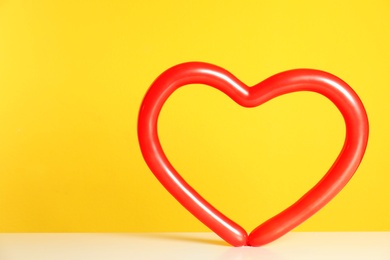 Photo of Heart figure made of modelling balloon on table against color background. Space for text
