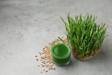 Photo of Glass of juice, sprouted wheat grass and grains on grey stone background. Space for text