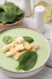 Photo of Delicious spinach cream soup with leaves and croutons in bowl on white wooden table, closeup