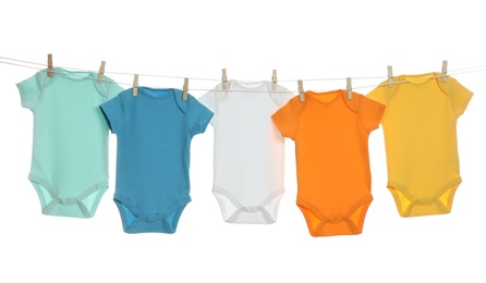 Photo of Colorful baby onesies hanging on clothes line against white background. Laundry day