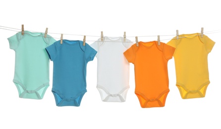 Colorful baby onesies hanging on clothes line against white background. Laundry day