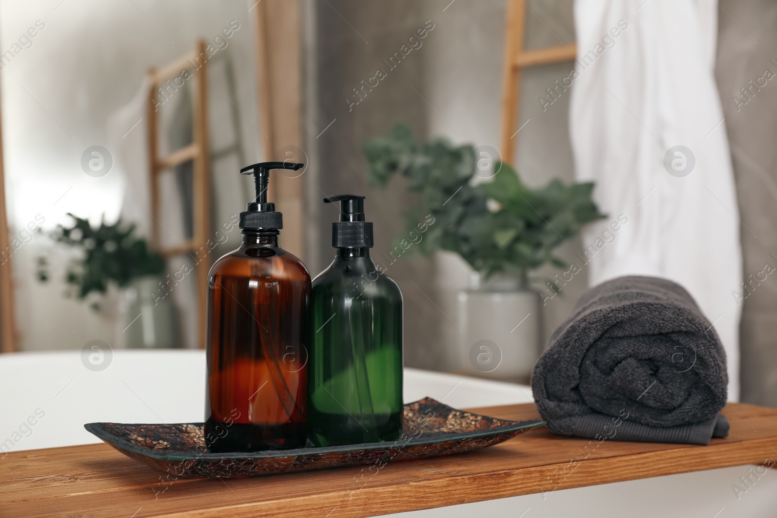 Photo of Wooden bath tray with bottles of shower gels and towel on tub indoors, space for text