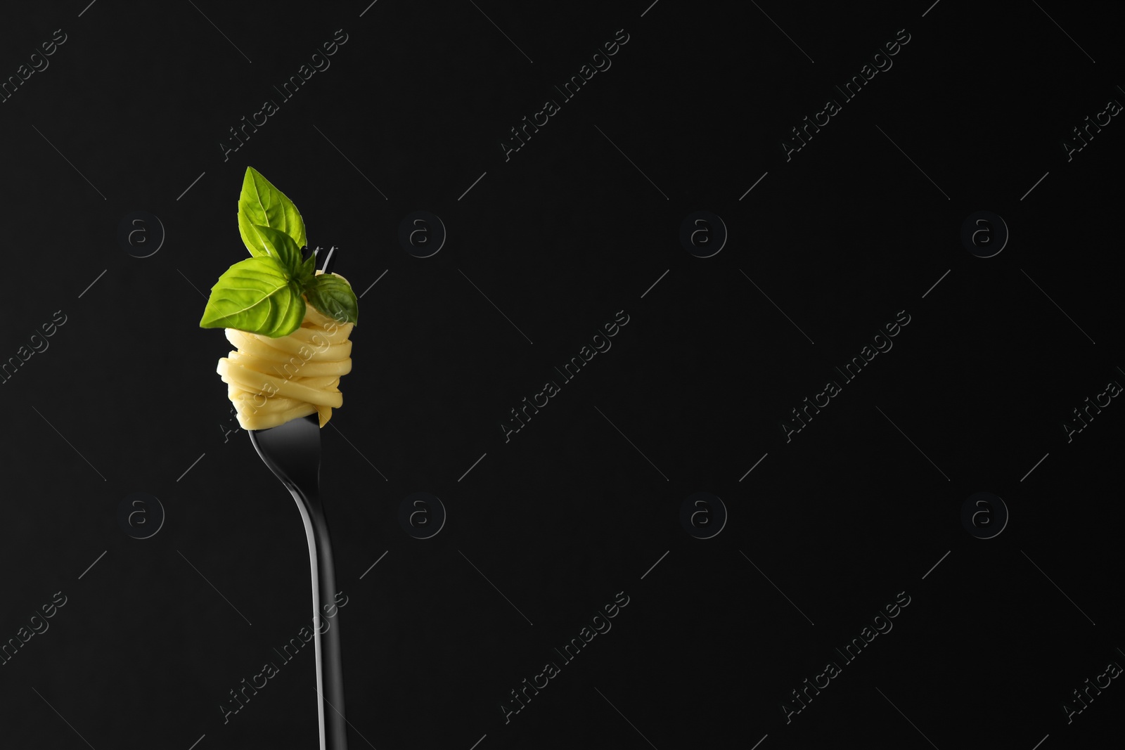Photo of Fork with tasty pasta and basil on black background, space for text