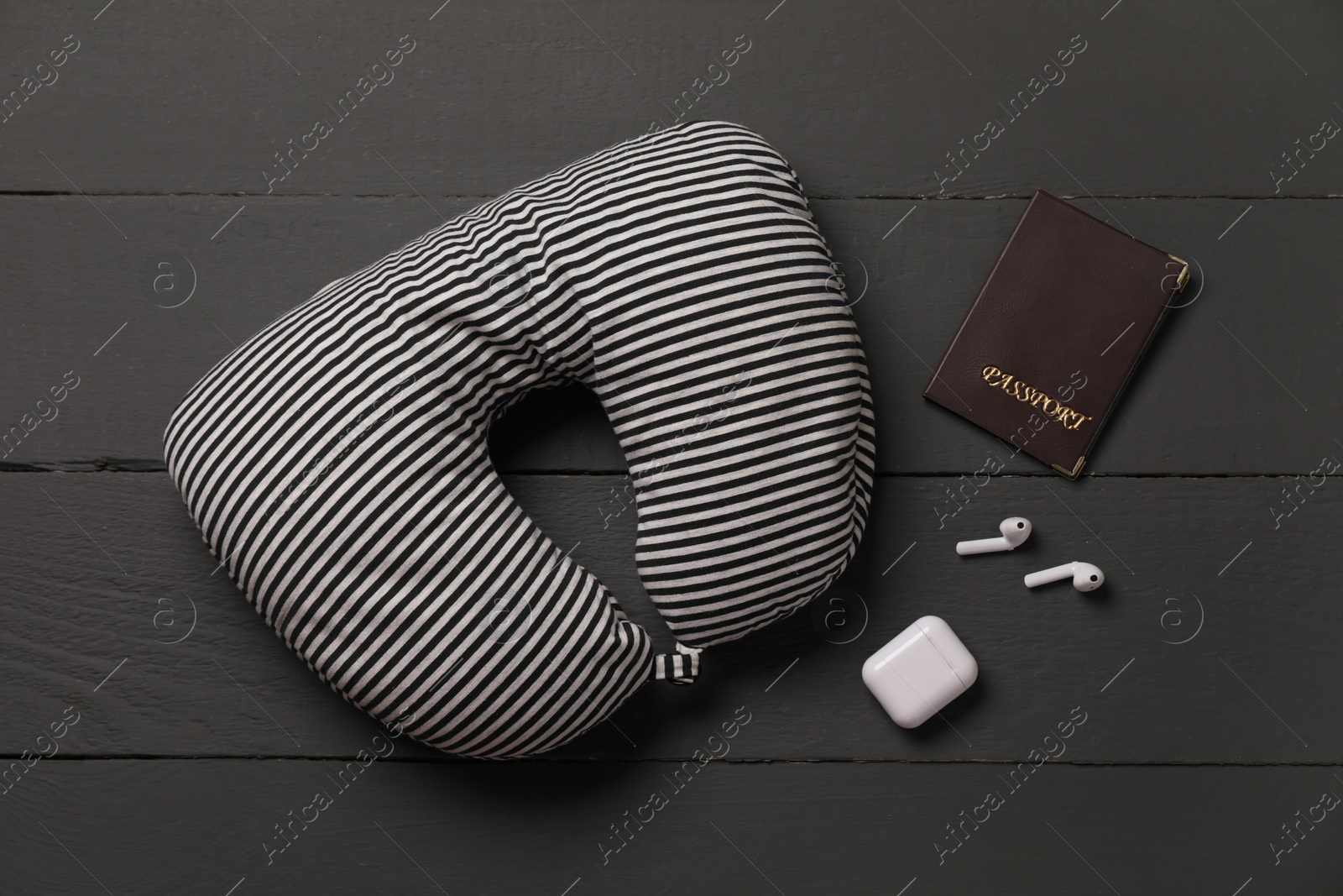 Photo of Striped travel pillow, passport and earphones on black wooden background, flat lay