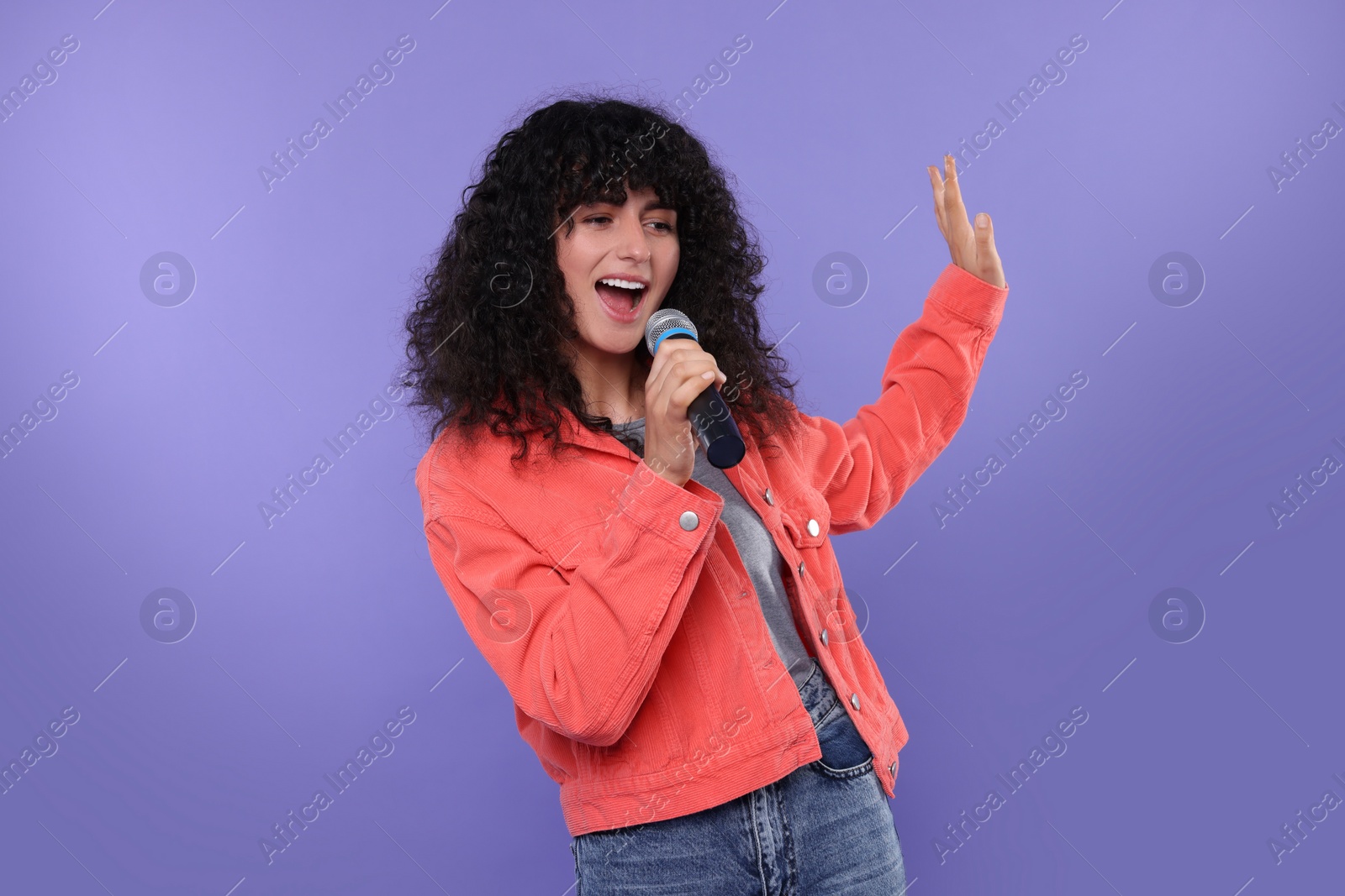 Photo of Beautiful young woman with microphone singing on purple background