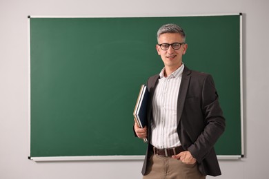 Teacher with notebooks near chalkboard in classroom, space for text