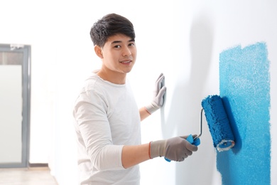 Male decorator painting wall with roller indoors