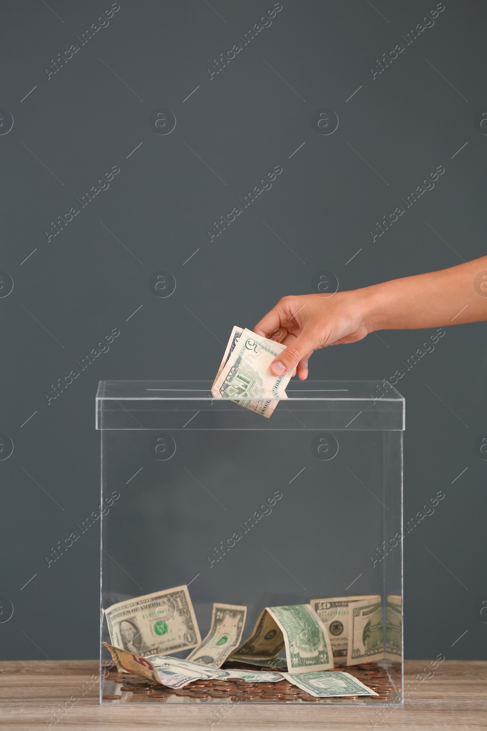 Photo of Woman putting money into donation box on table against grey background, closeup