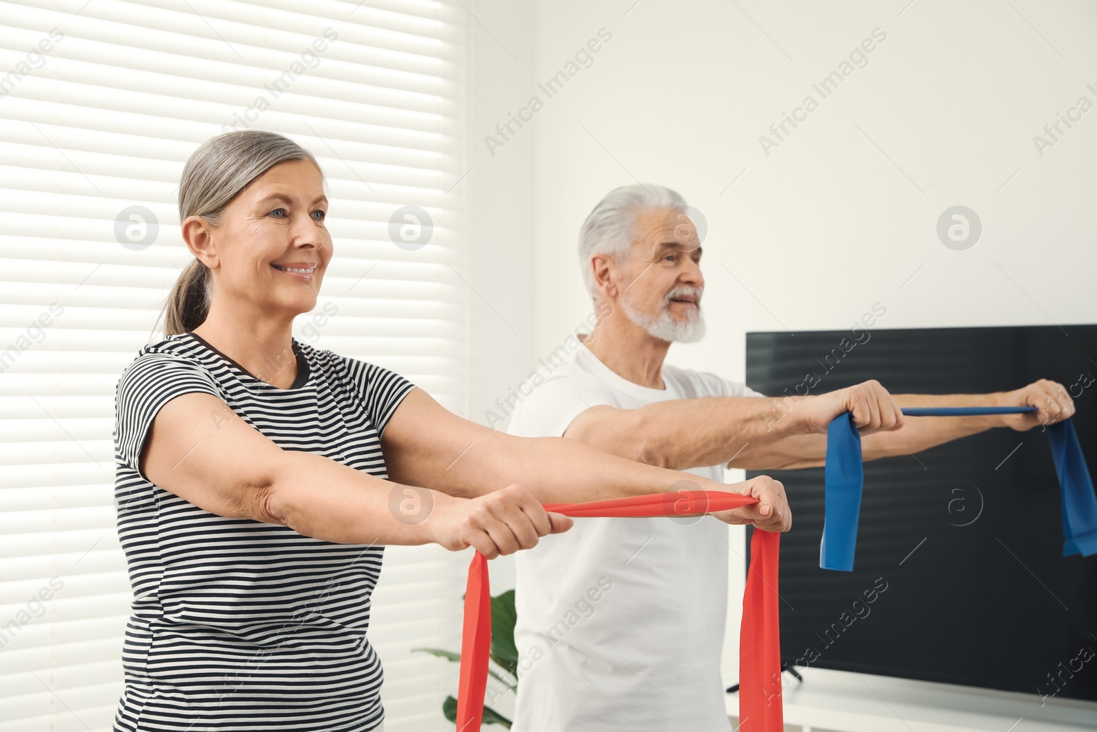 Photo of Senior couple doing exercise with fitness elastic bands at home, selective focus