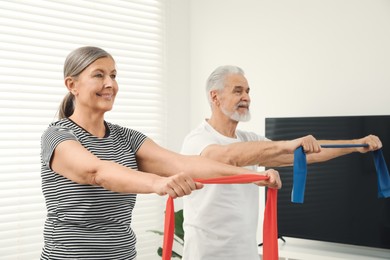 Senior couple doing exercise with fitness elastic bands at home, selective focus