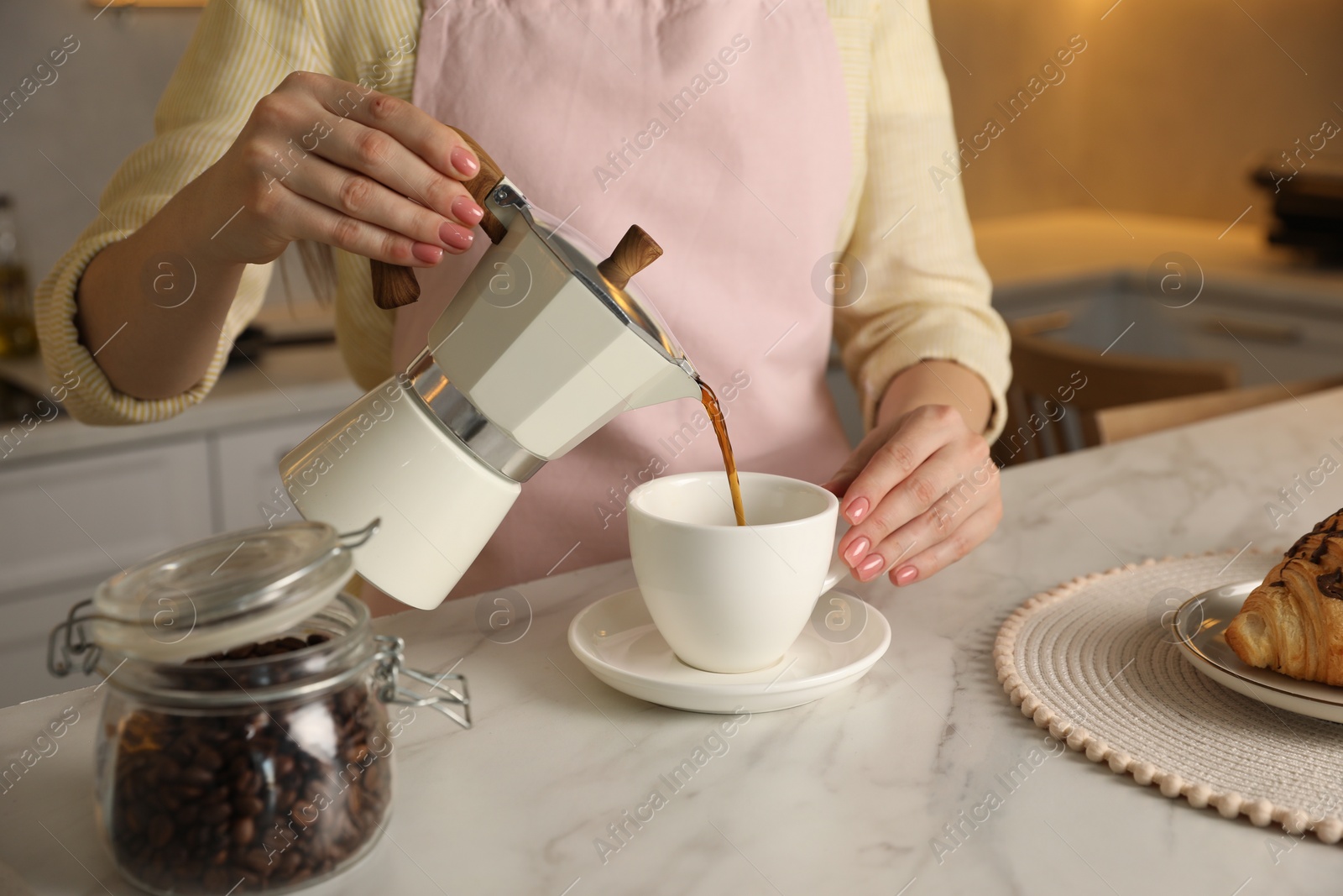 Photo of Woman pouring aromatic coffee from moka pot into cup at white marble table, closeup