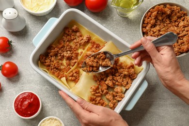 Photo of Woman making lasagna at light grey textured table, top view