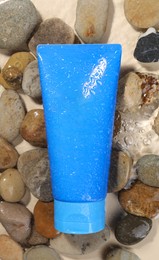 Tube of face cleansing product and stones in water against beige background, flat lay