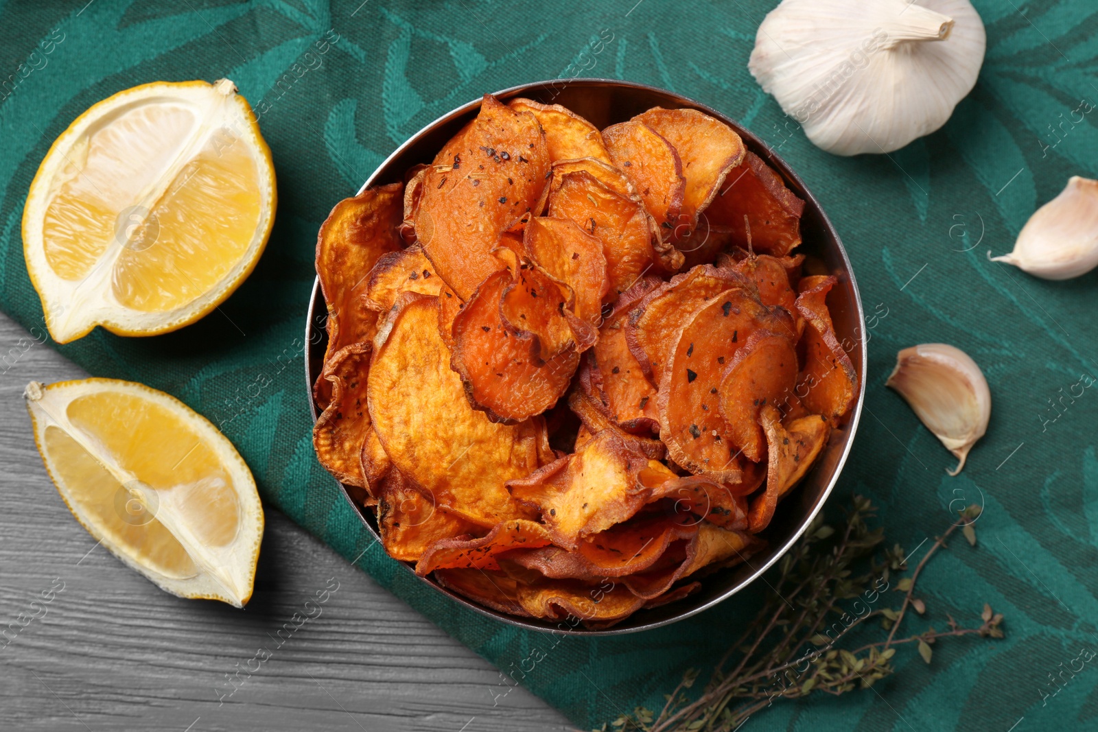 Photo of Bowl of sweet potato chips with lemon and garlic on table, flat lay