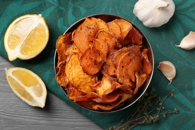 Photo of Bowl of sweet potato chips with lemon and garlic on table, flat lay