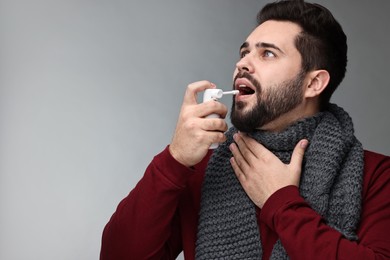 Photo of Young man with scarf using throat spray on grey background