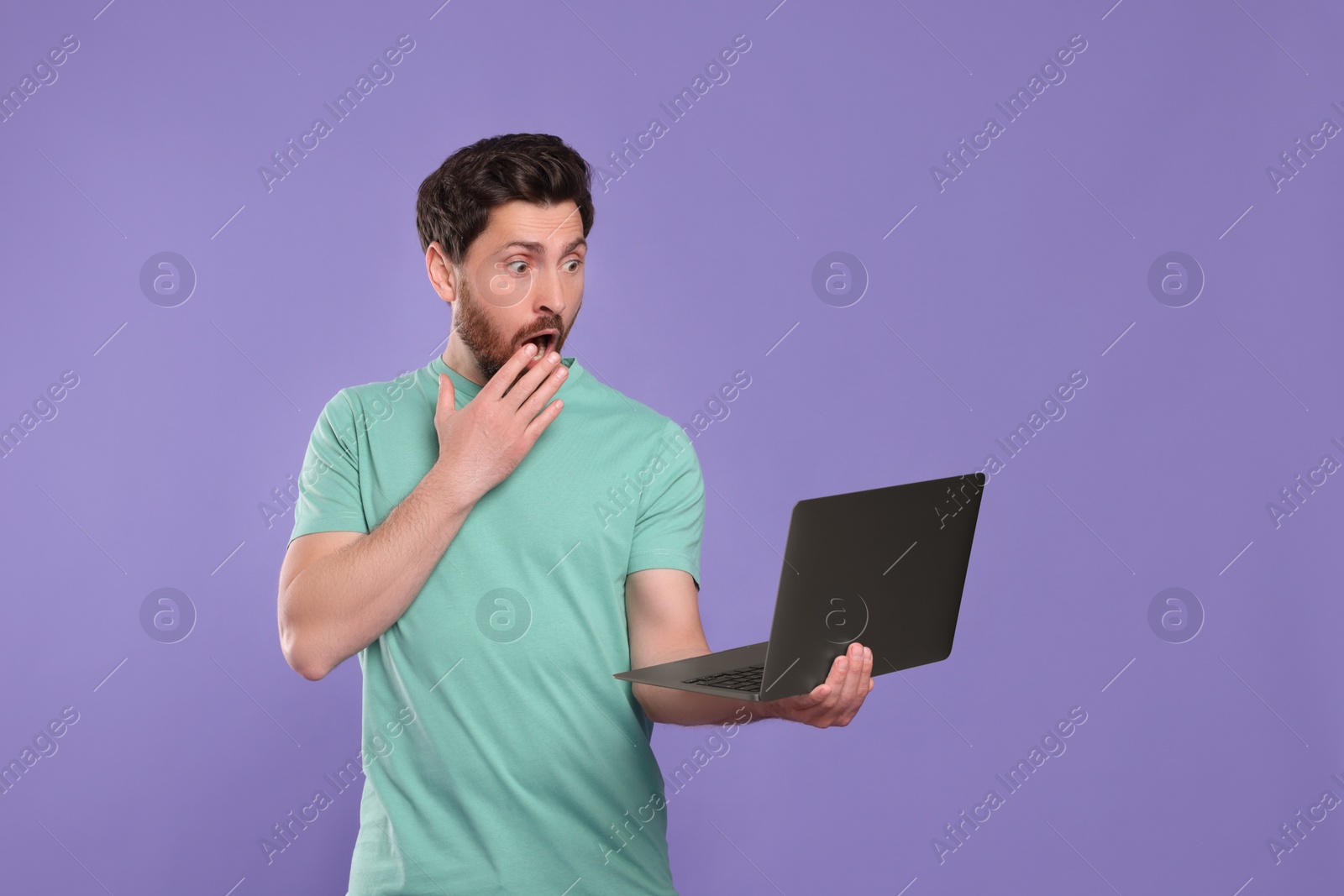 Photo of Emotional man with laptop on purple background. Space for text