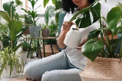 Photo of Houseplant care. Woman watering beautiful potted monstera with water indoors, closeup