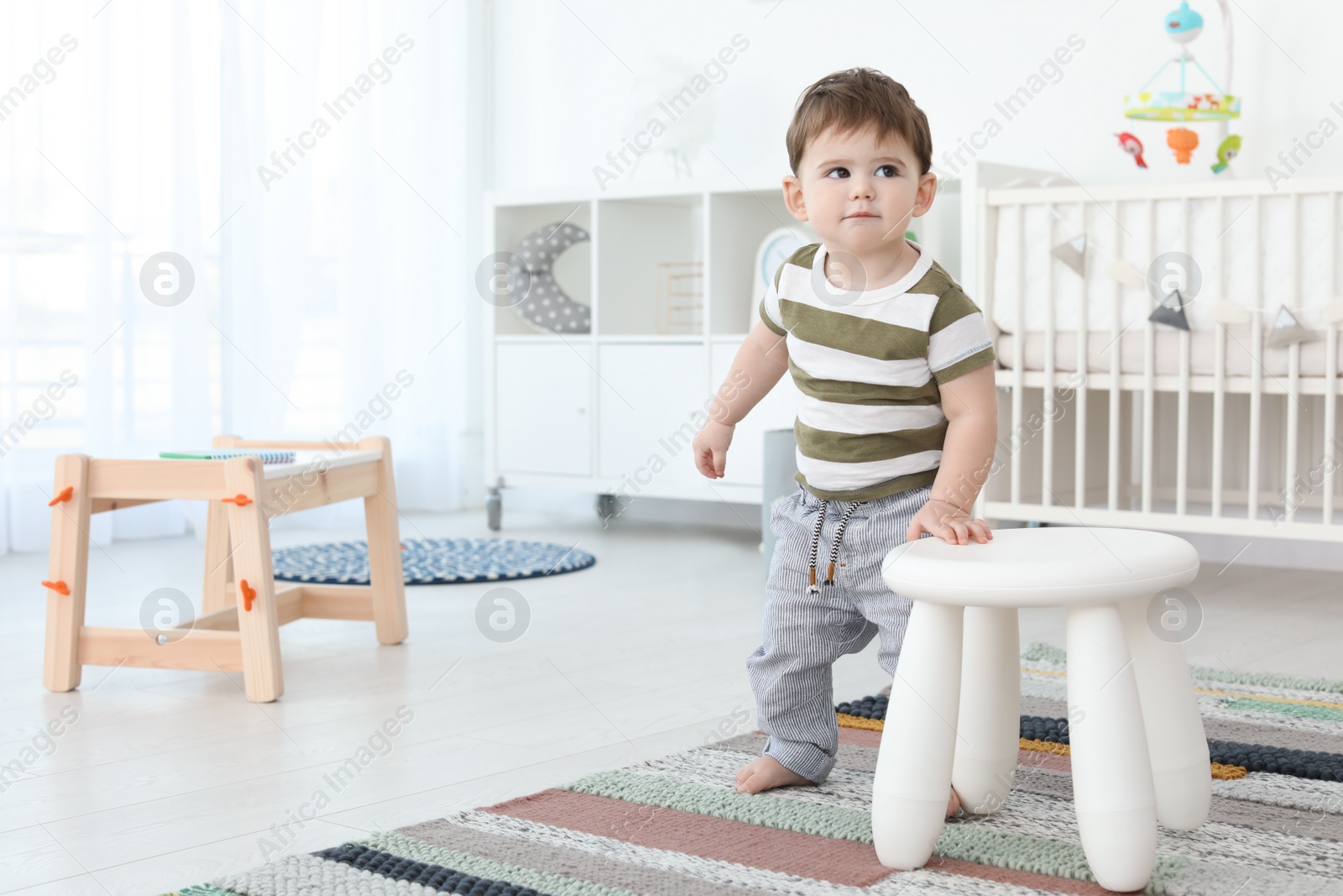 Photo of Cute baby holding on to stool at home.  Learning to walk