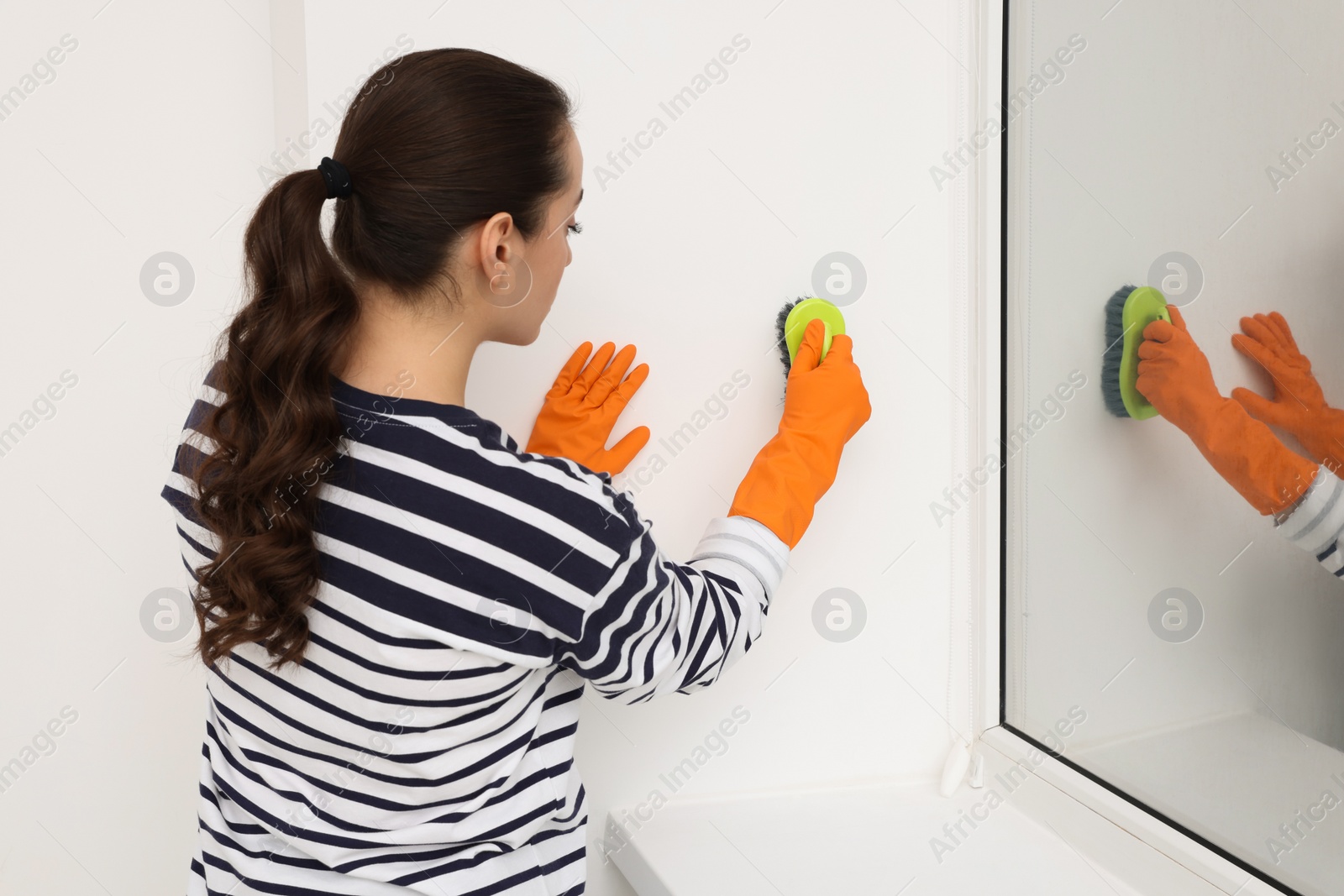 Photo of Woman in rubber gloves cleaning wall with brush indoors