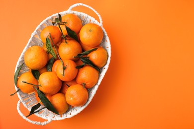 Photo of Fresh ripe tangerines and leaves in basket on orange table, top view. Space for text