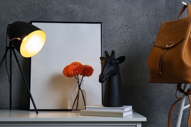 Photo of Stylish decor, vase with flowers, picture and desk lamp on white table near grey wall in hallway. Interior design