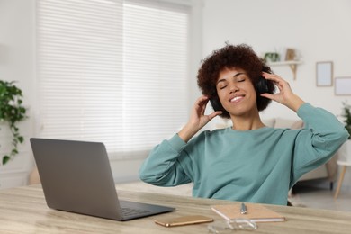 Young woman in headphones using laptop at wooden desk in room