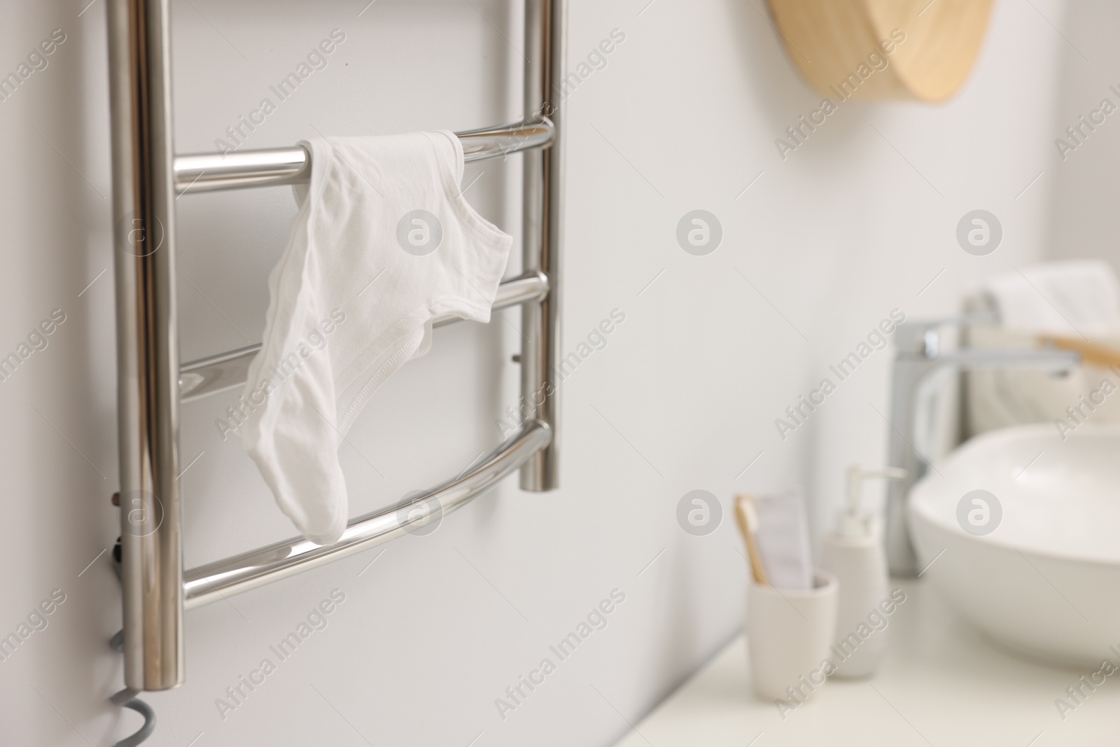 Photo of Heated towel rail with underwear on white wall in bathroom, closeup