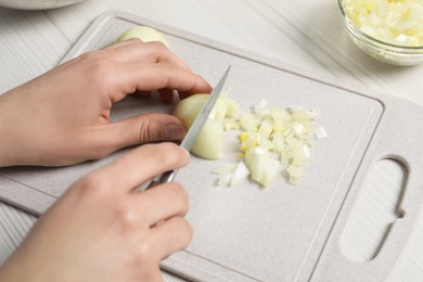 Photo of Woman cutting onion at white wooden table, closeup. Cooking vinaigrette salad