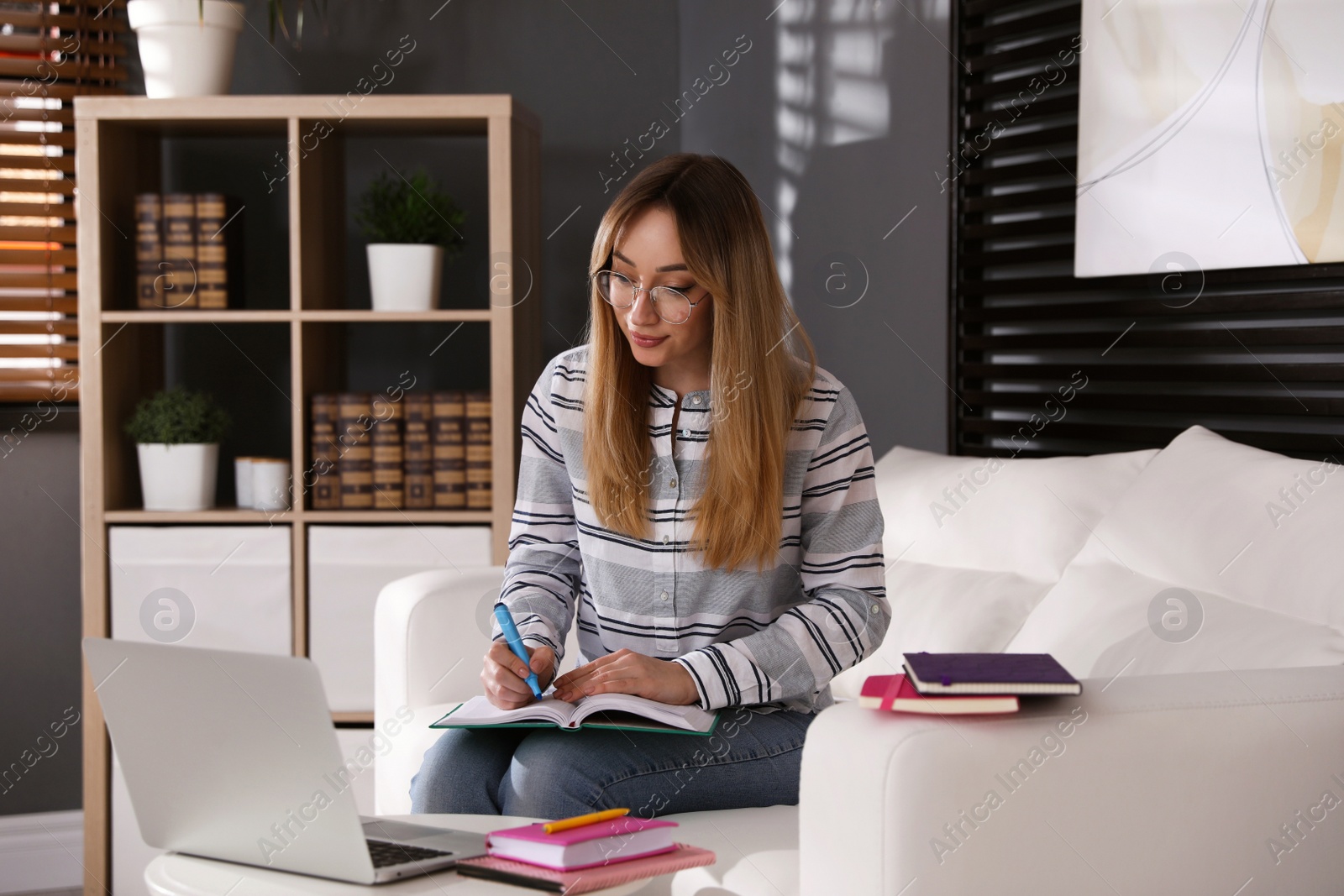 Photo of Young woman writing down notes during webinar at home