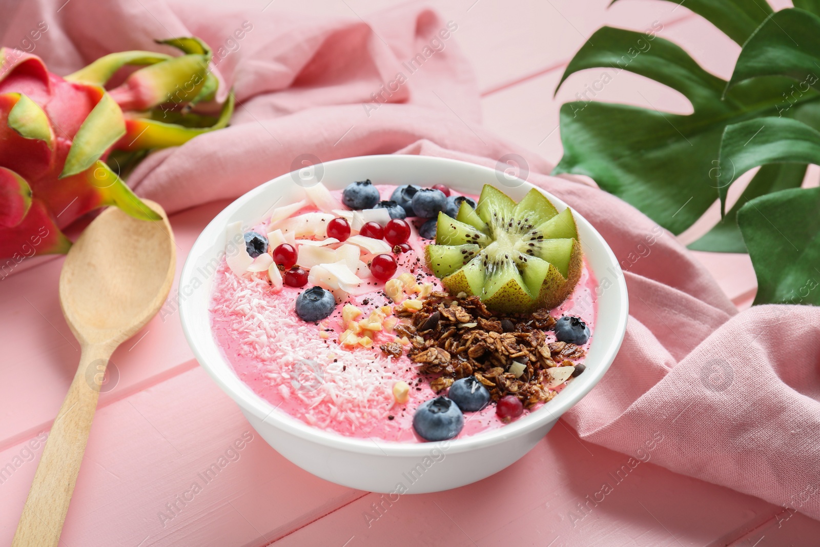 Photo of Tasty smoothie bowl with fresh kiwi fruit, berries and granola on pink wooden table