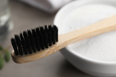 Photo of Bamboo toothbrush and bowl of baking soda on grey table, closeup