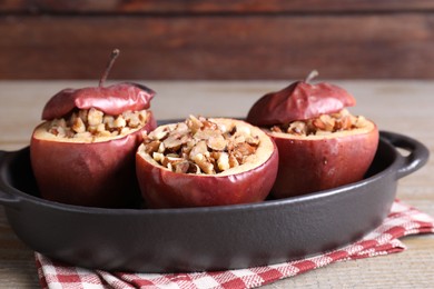 Tasty baked apples with nuts in baking dish on wooden table, closeup