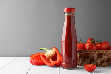 Photo of Bottle of tasty ketchup, tomatoes and pepper on white wooden table. Space for text