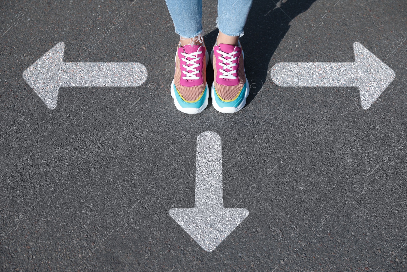 Image of Choice of way. Woman standing in front of drawn marks on road, closeup. White arrows pointing in different directions