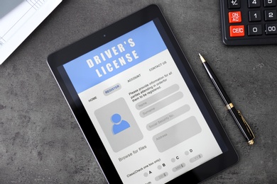 Photo of Tablet with driver's license application form, pen and calculator on grey table, flat lay