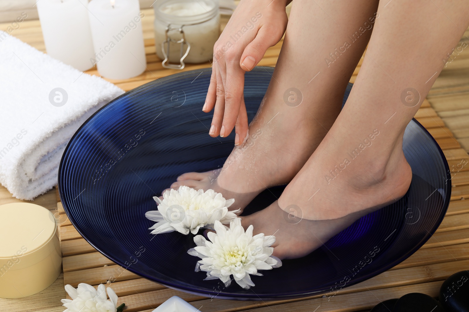 Photo of Woman soaking her feet in bowl with water and flowers on floor, closeup. Spa treatment