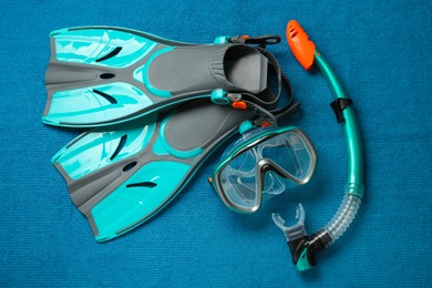 Photo of Pair of turquoise flippers and mask on blue fabric, flat lay