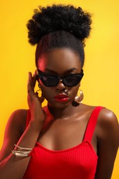 Fashionable portrait of beautiful woman with stylish sunglasses on yellow background