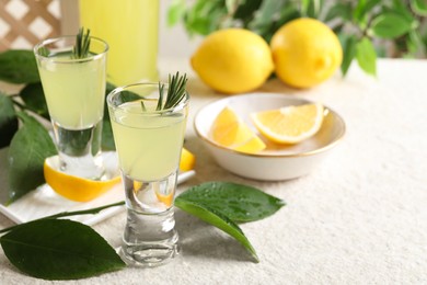 Photo of Tasty limoncello liqueur, lemons and green leaves on white textured table, closeup. Space for text