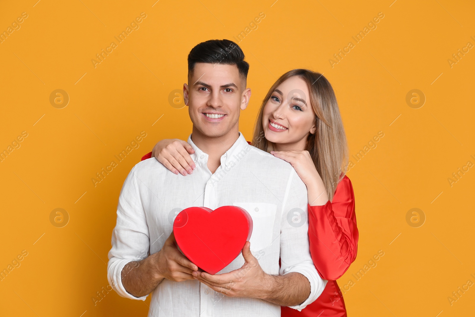 Photo of Lovely couple with decorative heart on yellow background. Valentine's day celebration