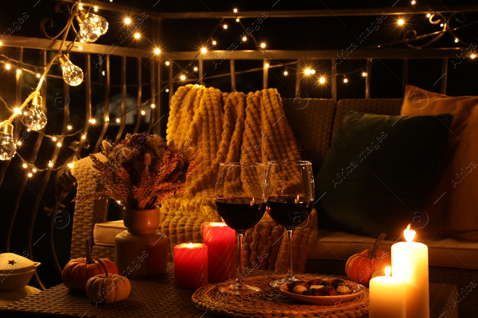 Photo of Glasses of wine, burning candles and decor on rattan table. Autumn evening on terrace