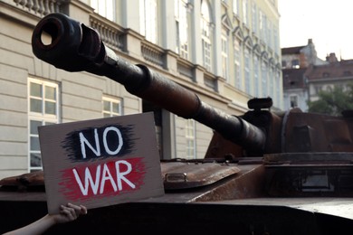 Photo of Boy holding poster with words No War near broken military tank on city street, closeup