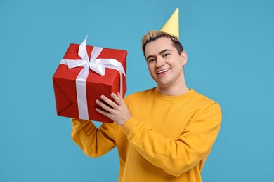 Young man with party hat and gift box on light blue background