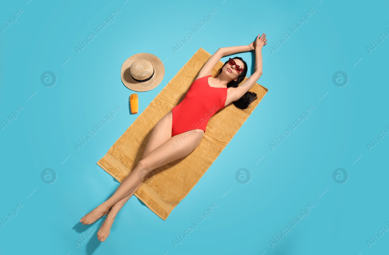 Photo of Young woman in stylish swimsuit on beach towel against light blue background