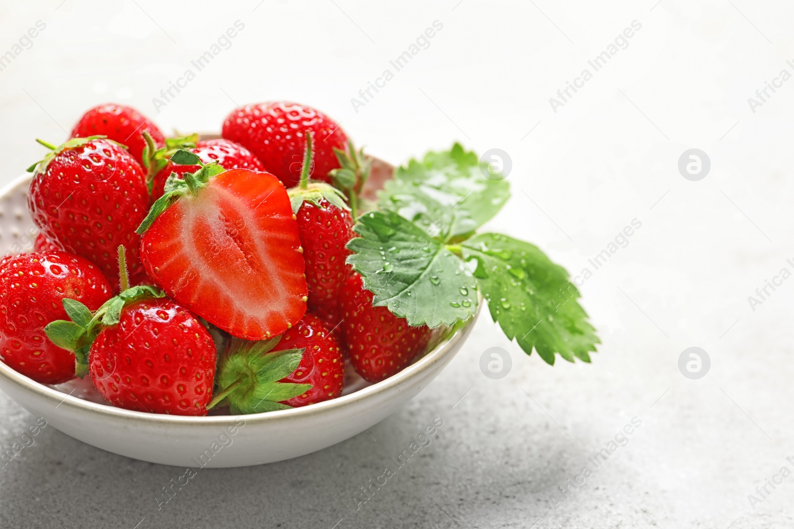 Photo of Bowl with ripe strawberries on light background