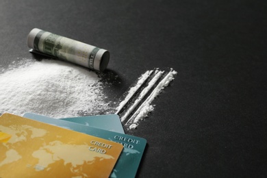 Composition with cocaine, credit cards and rolled dollar banknote on black background